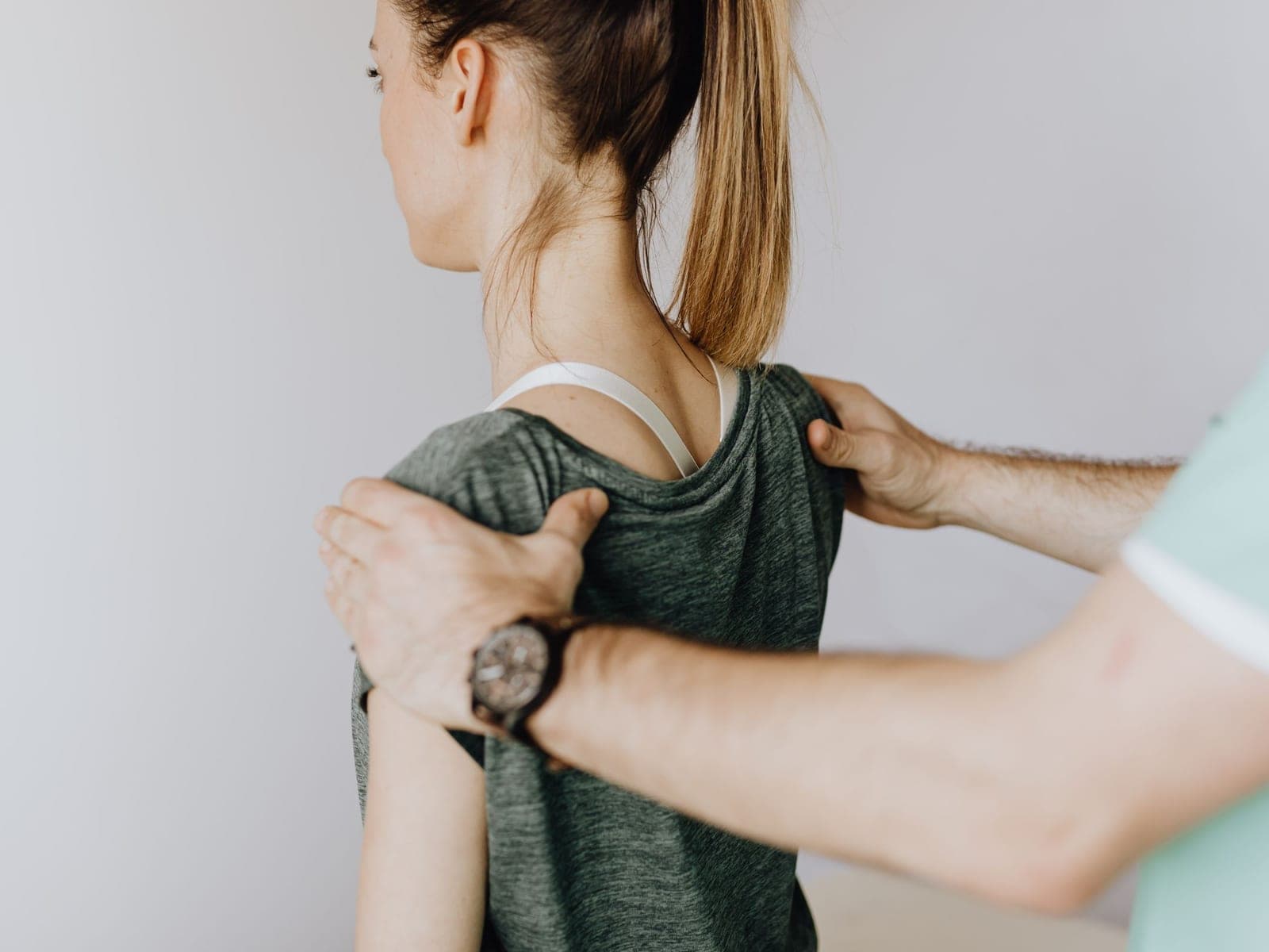 A practitioner examining a patient's shoulder from behind