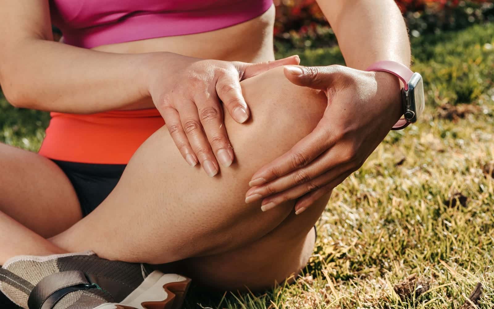 A runner sitting on the grass holding her knee
