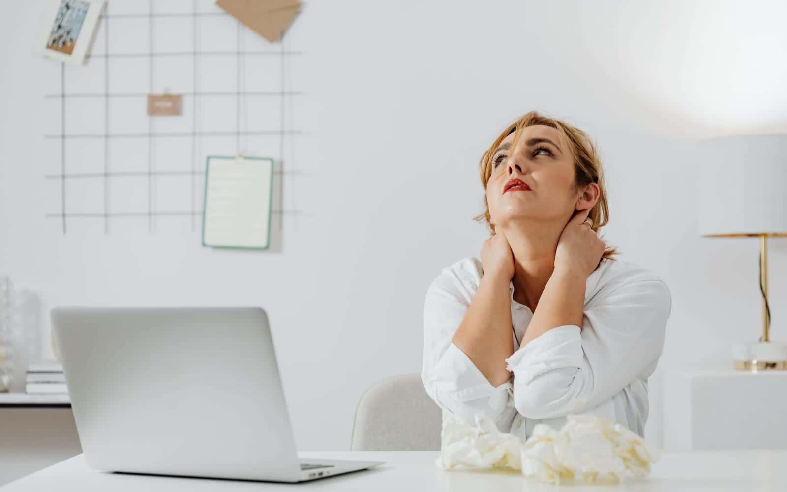 A woman at a desk with a laptop holding both sides of her neck