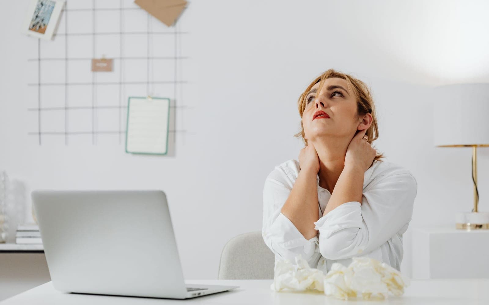 A woman at a desk with a laptop holding both sides of her neck