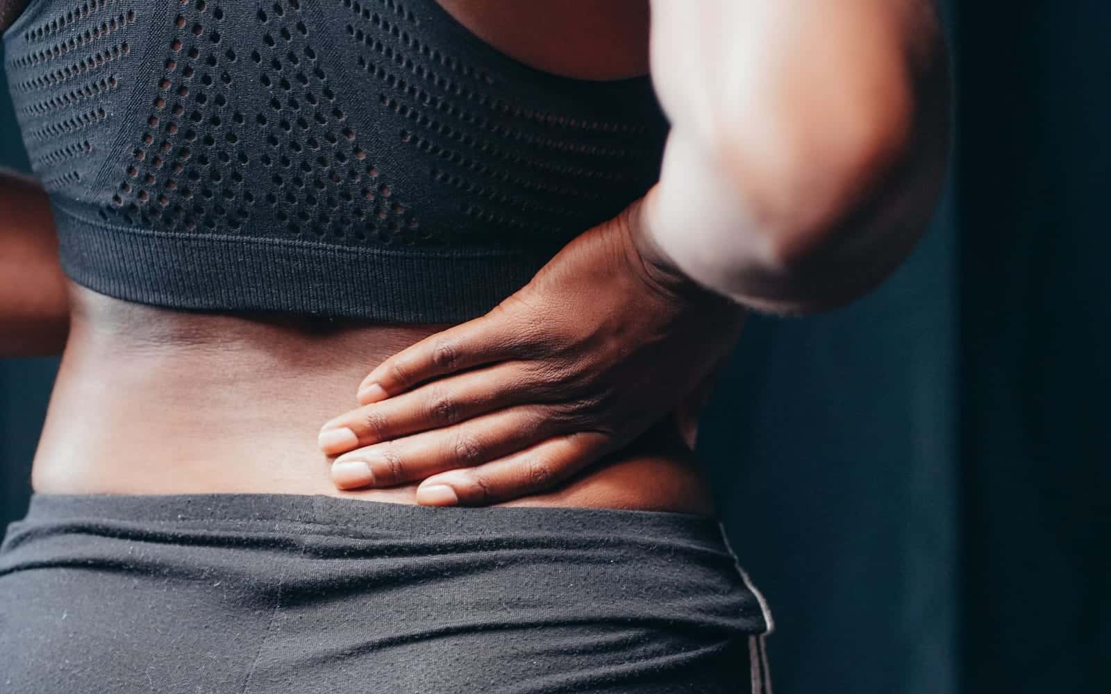 A woman in sportswear pressing a hand into her lower back