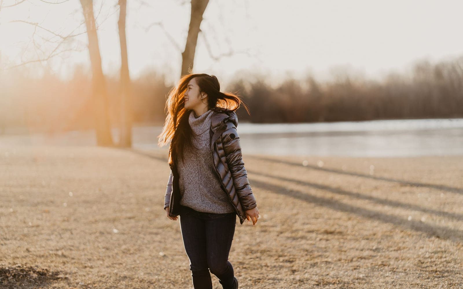 A woman in a winter coat walking through a sunny park on a cold, bright day