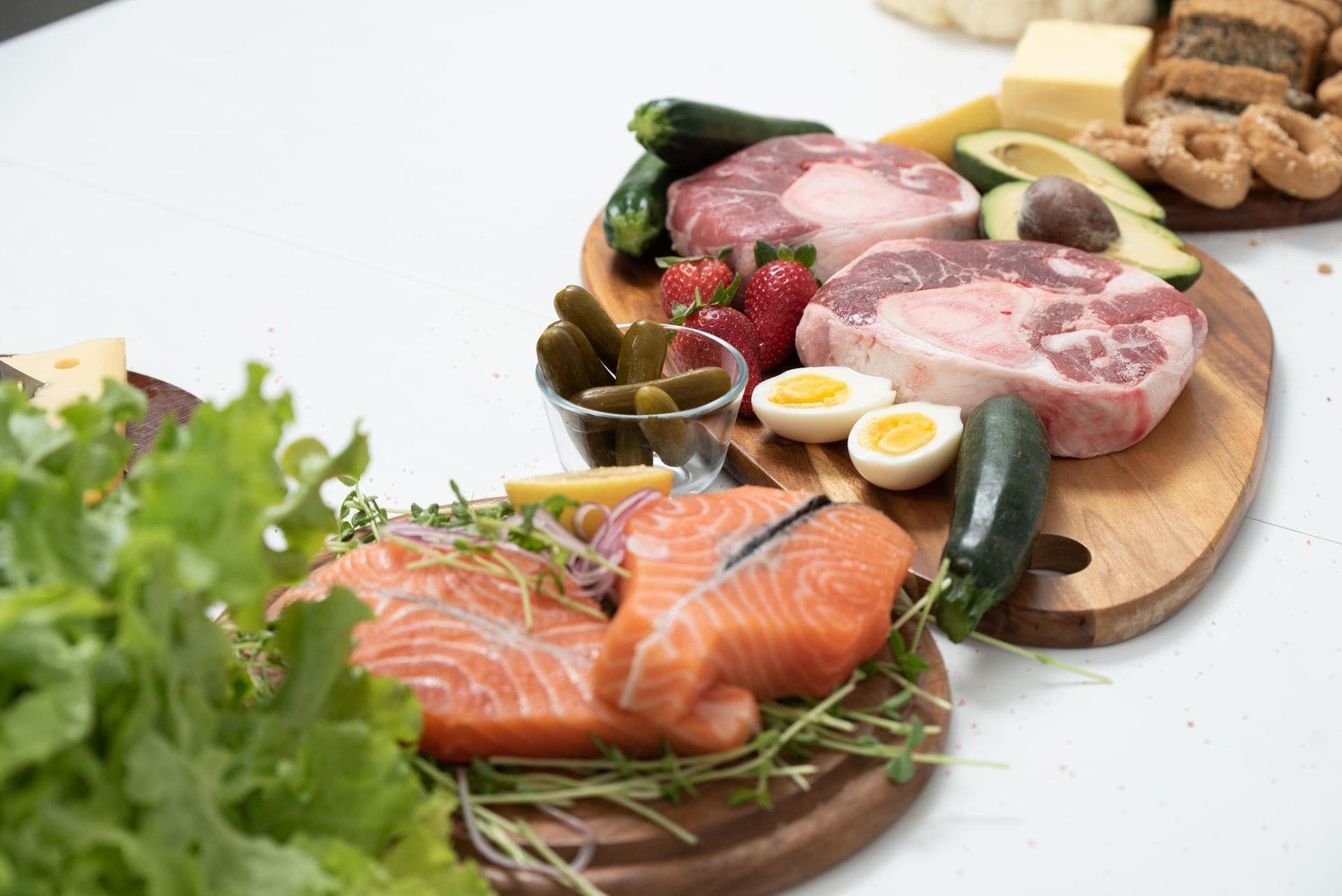 Salmon, beef, eggs, cheese and fresh vegetables on wooden boards